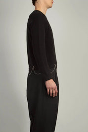 Black crew neck knit by Random Identities featuring 1x1 rib trims and chain detail at hem, styled with tailored trousers